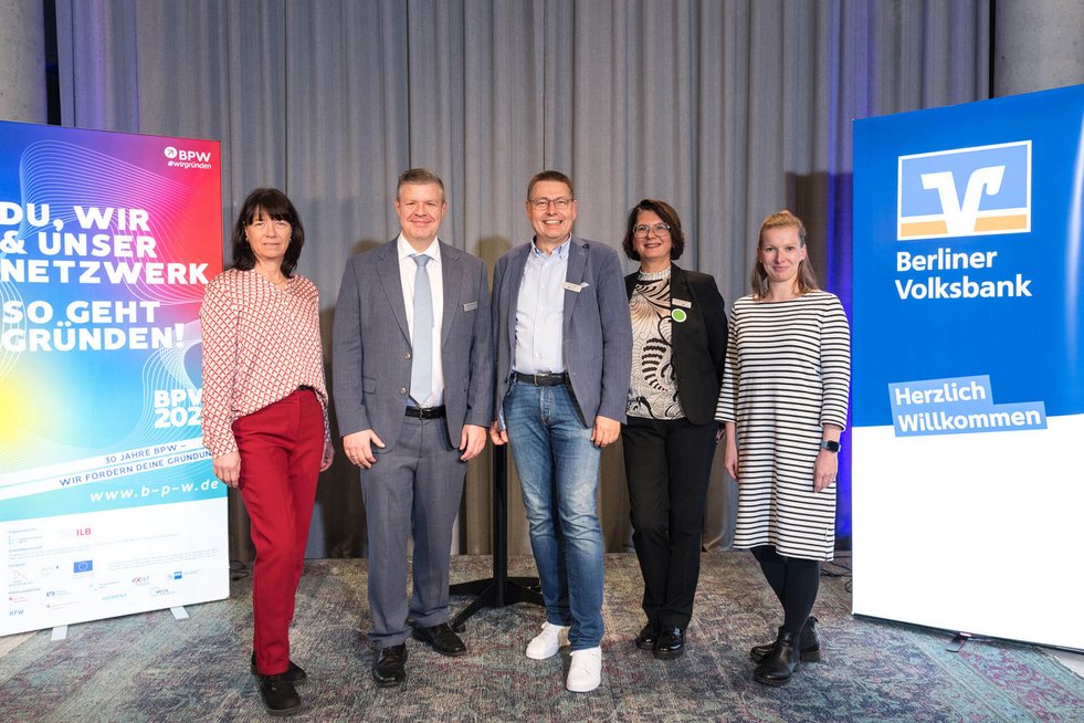 Fünf Personen stehen für ein Gruppenfoto zusammen auf einer Bühne