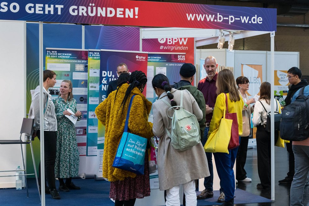 Menschen stehen an einem Messestand und unterhalten sich