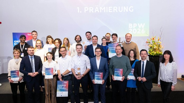 Große Gruppe von Personen auf einer Bühne bei einer Preisverleihung. Mehrere Teilnehmende halten Urkunden und Trophäen. Im Hintergrund ist die Aufschrift „1. Prämierung BPW 2026“ zu sehen.