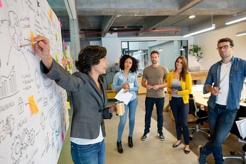 Frau steht an einer Tafel und spricht zu einer Gruppe von Menschen